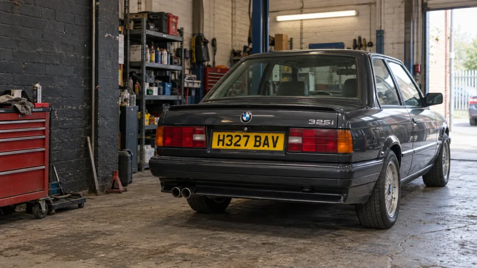 Graphite BMW 325i in a British workshop, with BMW badge and yellow UK registration plate H327 BAV